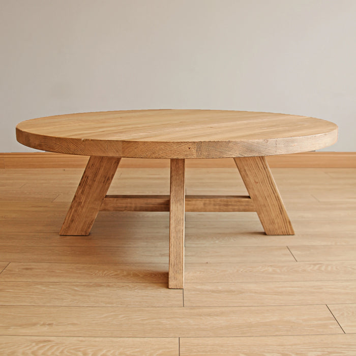 Low-angle view of the round coffee table, emphasizing the unique leg design and solid structure, without any decor or background distractions.