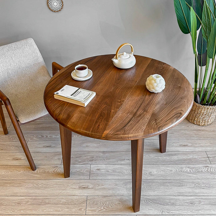 Angle shot of the petra round wood dining room table in a dining room, paired with neutral-colored chairs.