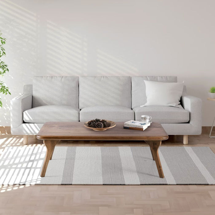Sidney Rectangular Cocktail Table made of solid walnut wood, featuring a mid-century modern design with clean lines and a rich wood finish side view with couch behind the product