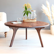 Sidney round solid walnut wood coffee table with sculptural curved legs in a bright minimalist living room