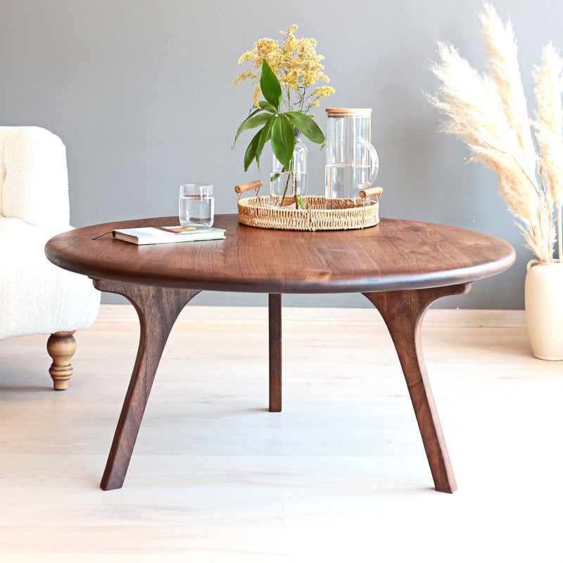 Sidney round solid walnut wood coffee table with sculptural curved legs in a bright minimalist living room
