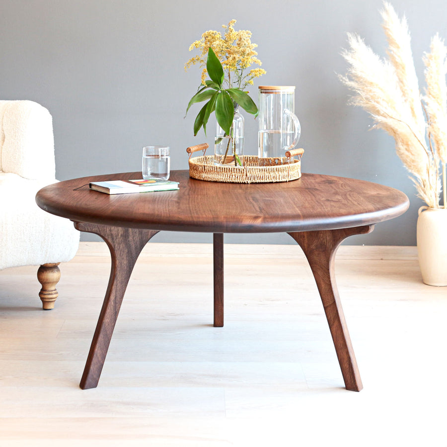 Sidney round solid walnut wood coffee table with sculptural curved legs in a bright minimalist living room