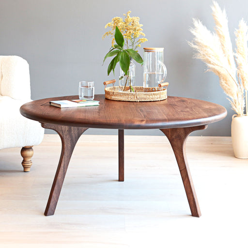Sidney round solid walnut wood coffee table with sculptural curved legs in a bright minimalist living room