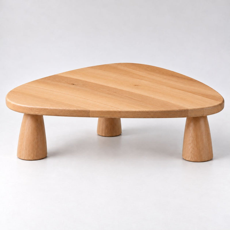 A triangular Yuma Organic Triangle Beech Wood Coffee Table with three tapered legs, shown on a clean light gray studio background.