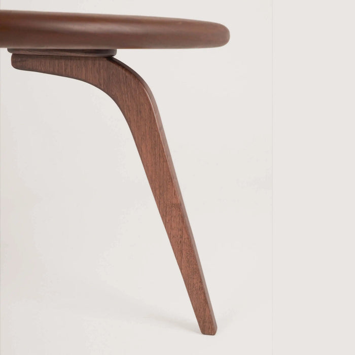 Close-up detail of one leg of the Aura Wood Cocktail Table, emphasizing the quality craftsmanship and rich grain of the solid walnut wood.