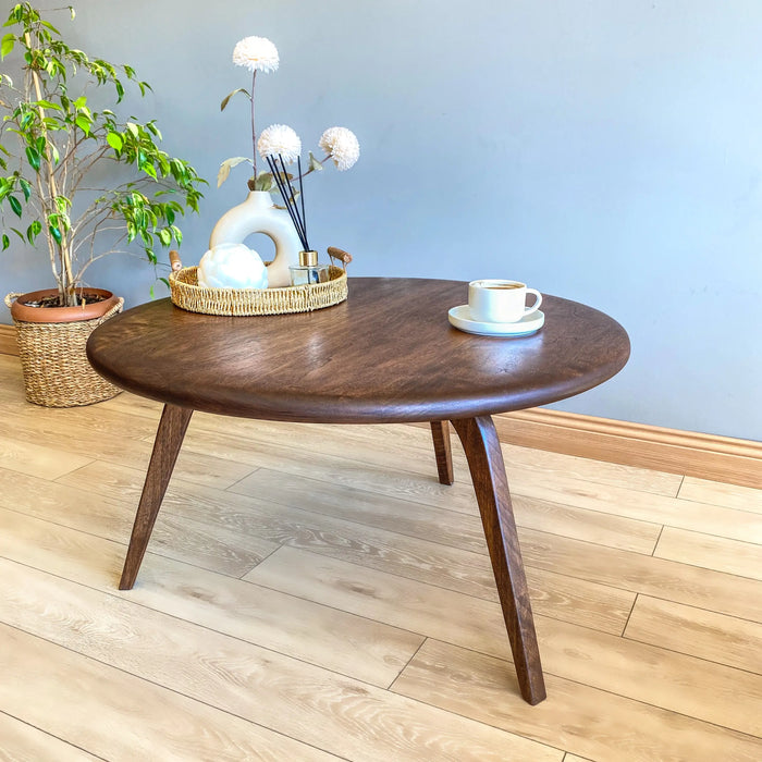 Right side view of the round coffee table in a cozy living space, adorned with decor items, emphasizing its stylish design and natural wood finish.