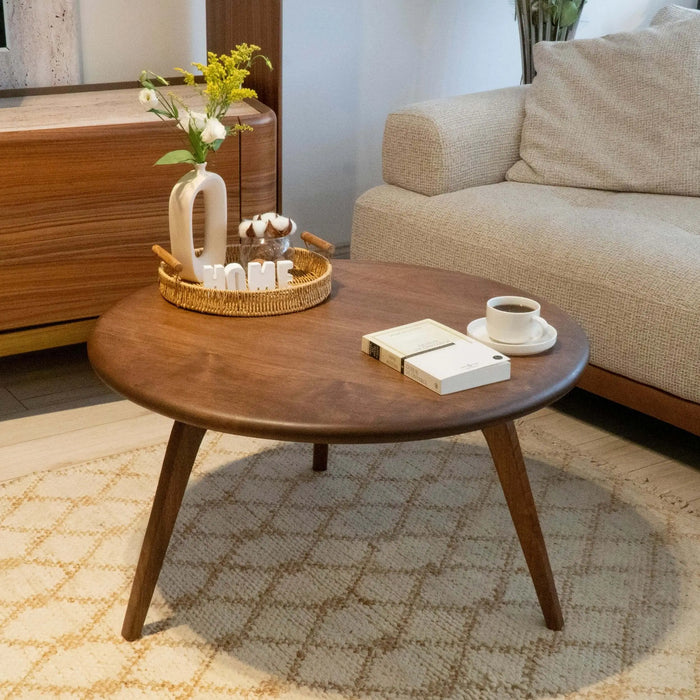 Front view of the round coffee table in a beautifully styled living room, with a cozy couch, plush carpet, and a TV unit in the background, showcasing its mid-century modern charm.