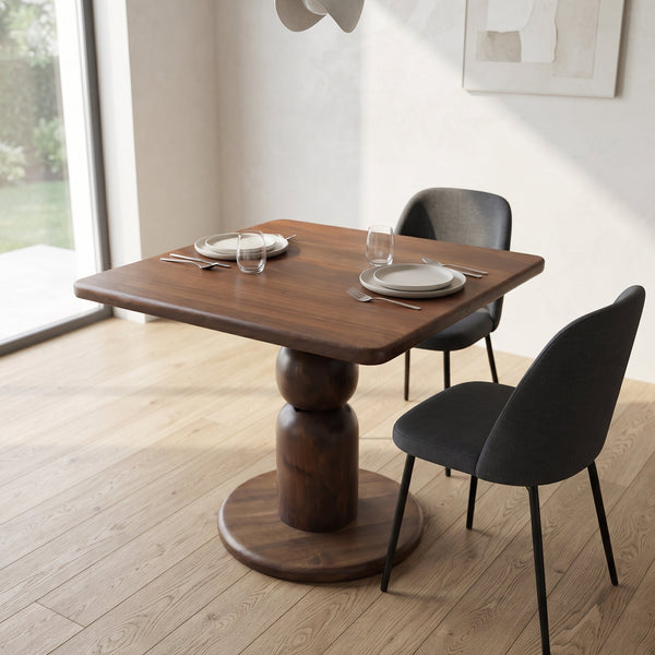 Dorel square walnut dining table with a round pedestal base and matching dark gray upholstered chairs, set in a bright modern room with light wood flooring and a large window.