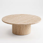 High three-quarter angle studio view of Dune Round Travertine Coffee Table displaying natural stone veining and cylindrical pedestal base