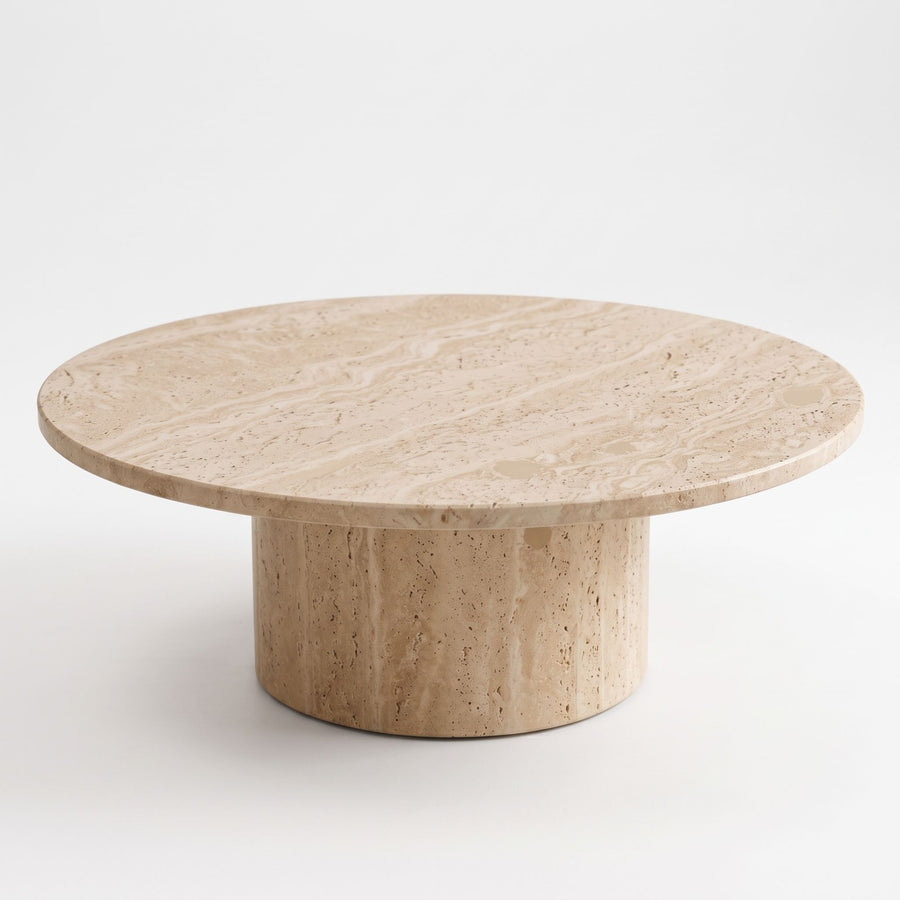 High three-quarter angle studio view of Dune Round Travertine Coffee Table displaying natural stone veining and cylindrical pedestal base