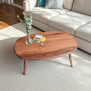 Elise Oval Coffee Table - Solid Walnut Wood with tapered legs, styled in a living room setting with a cream sofa, textured rug, and decorative items on top.