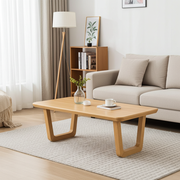 Lucia Solid Beech Wood Rectangular Coffee Table with sculptural angled legs in a modern living room setting, styled with a small vase of greenery, a white cup, and a coaster on a textured rug.