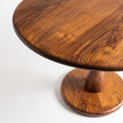 A close-up studio shot of Mason Solid Walnut Round Pedestal Dining Table | Sculptural Base
 with a rich warm brown finish and visible wood grain, set against a plain white background.