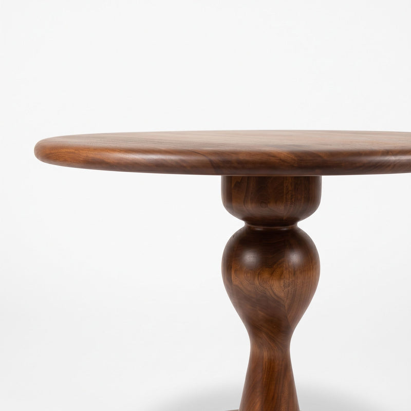 A close-up of Mason Solid Walnut Round Pedestal Dining Table | Sculptural Base
 table top and turned pedestal leg in a warm medium-to-dark brown finish, set against a plain white background.