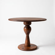 Mason Solid Walnut Round Pedestal Dining Table | Sculptural Base
 with a dark brown finish, featuring a turned stem base and a circular foot, photographed on a seamless white background.