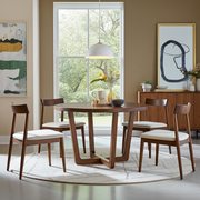 Muse Round Dining Table Set For 4 | Walnut Wood Design consisting of a round dark wood table and four matching chairs with white upholstered seats, arranged on a round light rug in a bright dining room.