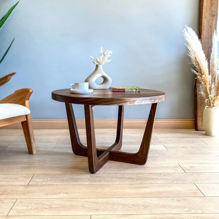Diagonal low-angle view of a solid walnut wood round coffee table, highlighting sturdy wooden legs and smooth tabletop finish.