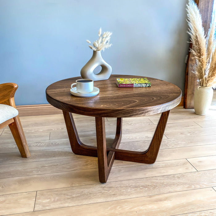 Diagonal top-angle view of a solid walnut wood round coffee table, highlighting sturdy wooden legs and smooth tabletop finish.