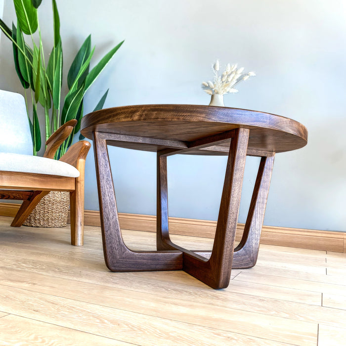 Low-angle view from beneath a solid walnut wood round coffee table, showcasing the underside structure and sturdy wooden legs.