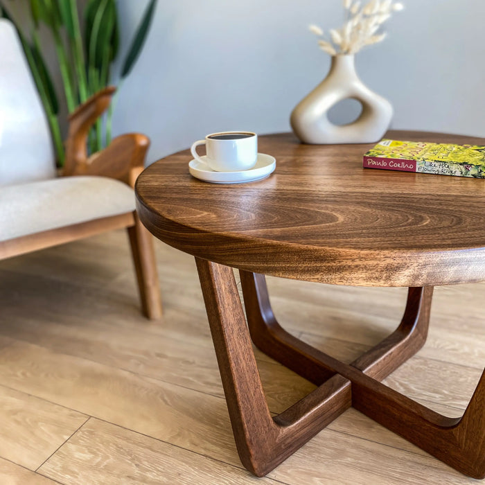 Close-up view of the left side of a solid walnut wood round coffee table, emphasizing the rich wood grain, smooth finish, and intricate details of the craftsmanship.