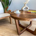 Close-up view of the left side of a solid walnut wood round coffee table, emphasizing the rich wood grain, smooth finish, and intricate details of the craftsmanship.