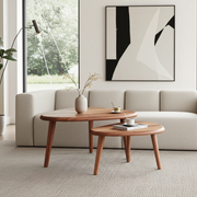 A modern living room scene featuring two nested Nova Mid-Century Modern Coffee Table Set - Solid Walnut Wood tables in front of a light beige sofa, with a large abstract black, white, and gray framed print on the wall behind.