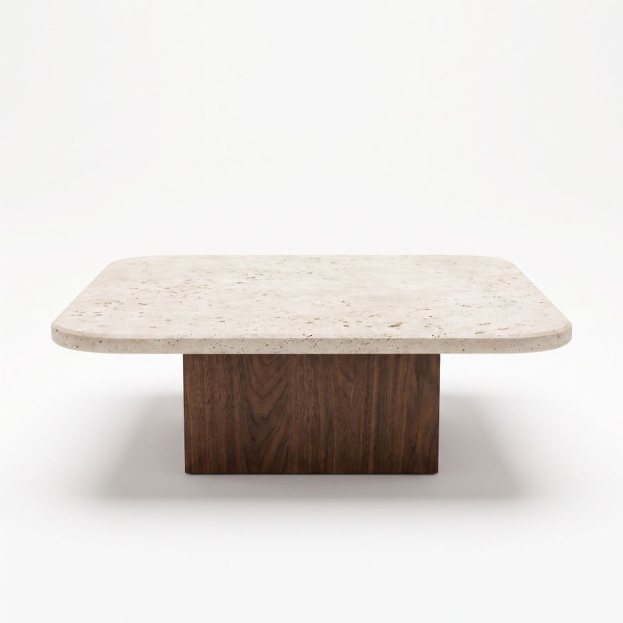 Eye-level straight-on studio shot of Pera Square Travertine Coffee Table featuring a rounded-corner beige stone top and solid walnut block base
