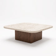 Three-quarter studio view of Pera Square Travertine Coffee Table featuring a rounded-corner beige stone top and solid walnut block base