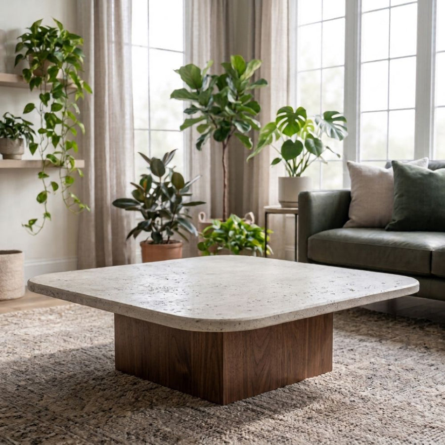 Pera Square Travertine Coffee Table with Solid Walnut Block Base Styled on Rug with Green Sofa and Indoor Houseplants in Bright Living Room