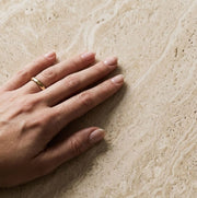 Detailed studio close-up showing human hand touching the porous texture and natural veining of beige travertine top on Pera Square Coffee Table
