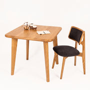 Petra Square Wood Dining Table Solid Oak Wood with four legs and a matching wooden chair with dark gray upholstered seat and backrest, set against a plain white background.