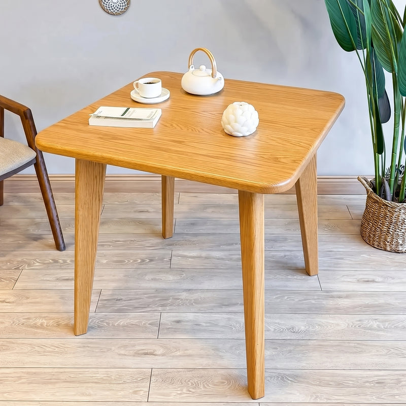 Petra Square Wood Dining Table Solid Oak Wood with rounded corners and tapered legs, styled with a white teapot, a cup and saucer, and a small decorative object on a light wood floor in a room setting.