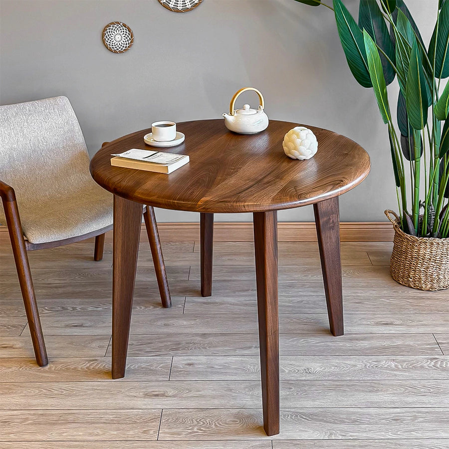 A round wood dining room table with a walnut finish, showcasing a sleek mid-century design in a modern dining space.