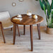 A round wood dining room table with a walnut finish, showcasing a sleek mid-century design in a modern dining space.