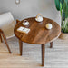 Angle shot of the petra round wood dining room table in a dining room, paired with neutral-colored chairs.