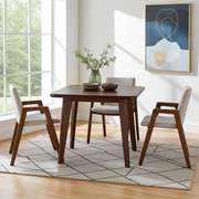 Petra Square Wood Dining Table | Walnut Wood Mid Century Design  featuring a dark brown wooden table and four matching armchairs with light beige upholstered seats, styled on a gray geometric rug in a bright, sunlit room.