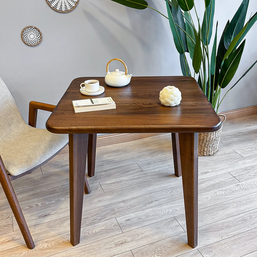 The Petra Square Wood Dining Table paired with minimalist dining chairs in a well-lit room, adding sophistication to any space.