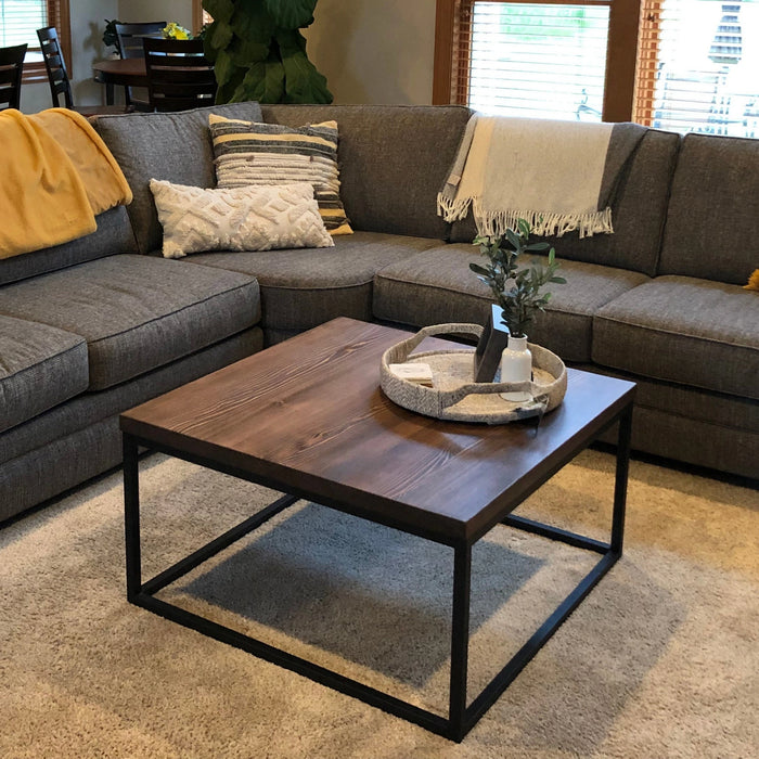 Renton square wooden coffee table in a living room, viewed from a diagonal angle, showcasing its design and setting.