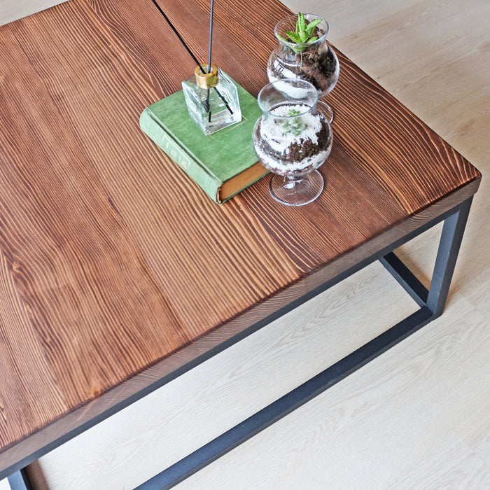 Detailed view of the right side of the Renton square wooden coffee table with decor, focusing on the tabletop and visible metal legs.