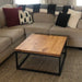 Customer photo of the square wood coffee table on a carpet, with a couch in the background in a living room setting.