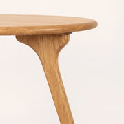 Close-up of Sidney Circular Dining Table Solid Oak Wood – Mid-Century Modern Design showing the rounded circular tabletop and a single tapered leg with a curved base, set against a plain off-white background.