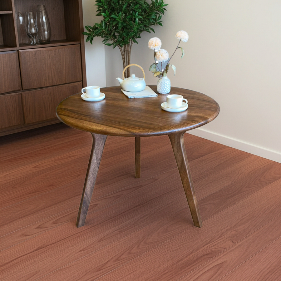 Sidney Circular Walnut Dining Table | Mid Century Modern with tapered legs, styled with a white teapot, two white teacups, and a small vase of flowers in a room with reddish-brown wood flooring.