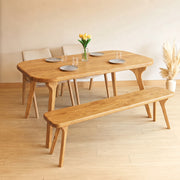 A light oak dining set featuring Sidney Rectangle Dining Table Solid Oak Wood – Mid-Century Modern Design, a matching bench, and three chairs, styled with plates, a vase of yellow tulips, and pampas grass in a minimalist room.