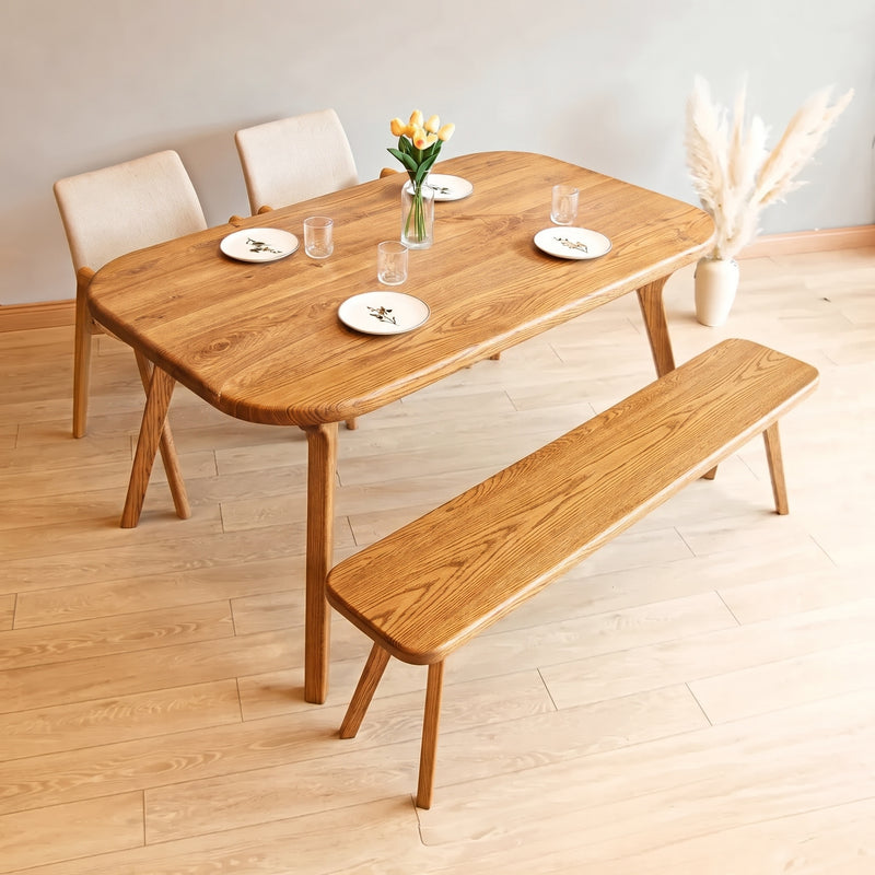 Sidney Rectangle Dining Table Solid Oak Wood – Mid-Century Modern Design with rounded corners, matching bench, and three upholstered chairs in a minimalist room with light wood floors.