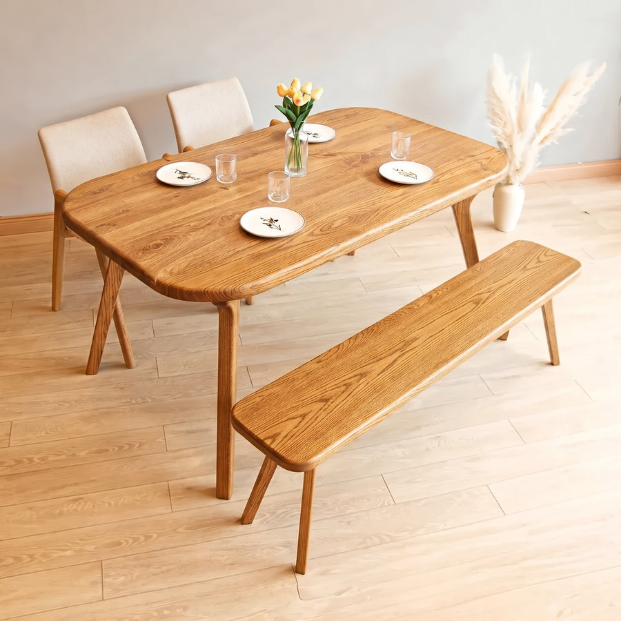 Sidney Rectangle Dining Table Solid Oak Wood – Mid-Century Modern Design with rounded corners, matching bench, and three upholstered chairs in a minimalist room with light wood floors.