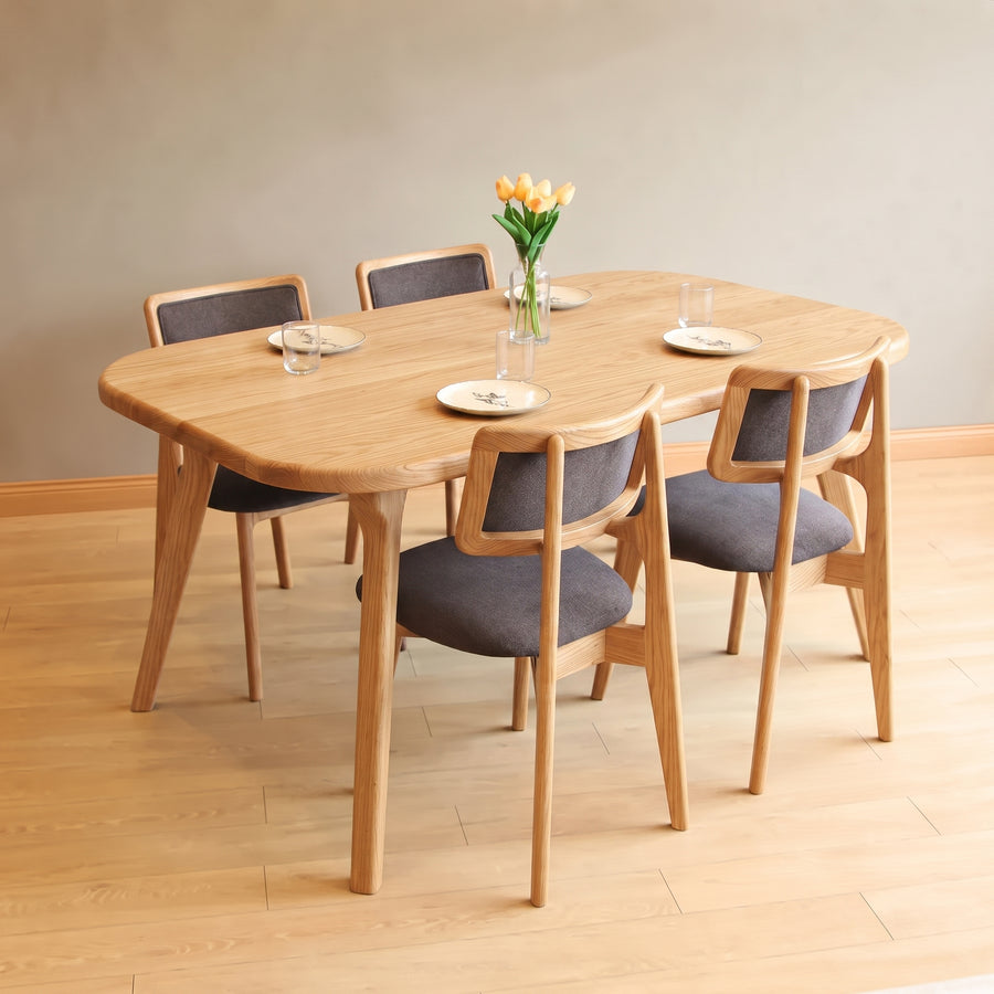 Sidney Rectangle Dining Table Solid Oak Wood – Mid-Century Modern Design with four matching chairs featuring gray upholstered seats and backs, styled with plates, glasses, and a vase of tulips in a minimalist room with light wood floors and a beige wall.
