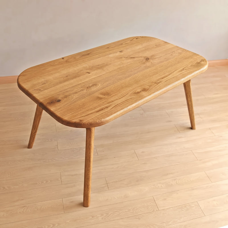 Sidney Rectangle Dining Table Solid Oak Wood – Mid-Century Modern Design with rounded corners and tapered legs, shown on a light wood plank floor against a neutral beige wall.