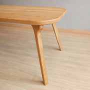 A close-up of Sidney Rectangle Dining Table Solid Oak Wood – Mid-Century Modern Design showing the rounded top edge and one of its tapered legs, set on a light wood floor against a neutral gray wall.