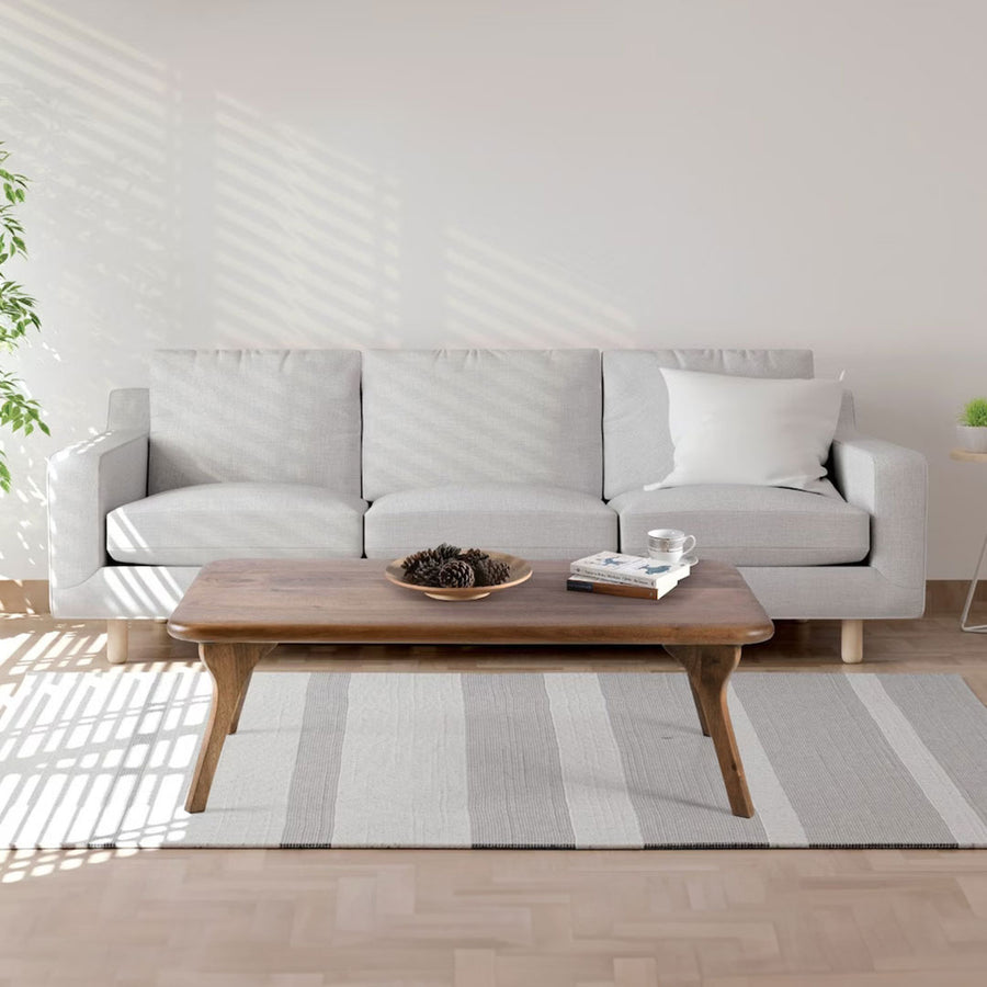 Sidney Rectangular Cocktail Table made of solid walnut wood, featuring a mid-century modern design with clean lines and a rich wood finish side view with couch behind the product 