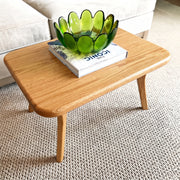 Sidney Rectangular Coffee Table Solid Oak Wood – Mid-Century Modern Design with rounded corners and tapered legs, styled with a green translucent flower-shaped bowl on top of a book in a living room setting.